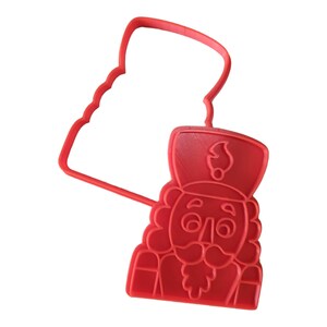Op de afbeelding: Een rode plastic koekjesuitsteker in de vorm van een notenkrakersoldaat. De uitsteker toont het gezicht, de hoed en het uniform van de soldaat. Het heeft een handvat voor gemakkelijk gebruik. Perfect voor feestelijke koekjes.
