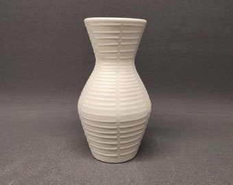 May include: White ceramic vase with a ribbed design. The vase has a narrow neck and a wide base.
