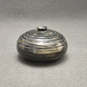 Może przedstawiać: Mały, okrągły, czarny i złoty ceramiczny wazon z fakturowaną powierzchnią.