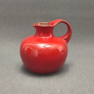 Può includere: Un piccolo brocca in ceramica rossa con corpo rotondo e manico marrone.