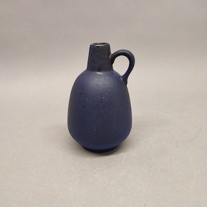 May include: A small, dark blue ceramic vase with a rounded body and a single handle. The vase has a textured surface.