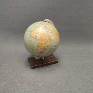Könnte beinhalten: Ein Vintage-Globus mit einem Holzsockel. Der Globus ist hellblau mit einer gelben und braunen Weltkarte. Der Globus steht auf einem dunkelbraunen Holzsockel.