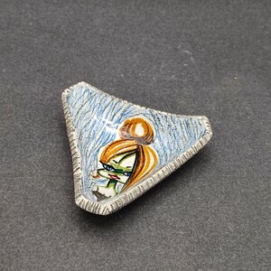 Può includere: Un piatto triangolare in ceramica con un motivo a strisce blu e bianche e un viso di cartone animato dipinto a mano con occhi verdi e capelli arancioni.