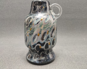 May include: A small, black and white glass vase with a clear glass handle. The vase has a swirling pattern with gold accents.