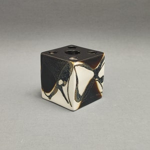 Può includere: Un vaso in ceramica bianca a forma di cubo con disegni astratti neri e marroni. Il vaso ha cinque aperture sulla parte superiore per i fiori.