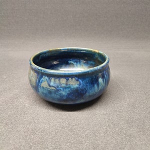 Könnte beinhalten: Eine kleine, blaue Keramikschüssel mit einer marmorierten Glasur. Die Schüssel hat eine abgerundete Form und einen leicht ausgestellten Rand.
