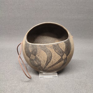 May include: A brown ceramic hanging planter with a black abstract design. The planter has a rope loop for hanging.