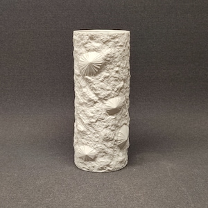 Puede incluir: Jarrón de cerámica blanca con superficie texturizada y diseños geométricos en relieve. El jarrón tiene forma cilíndrica.