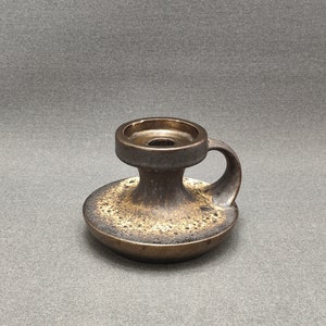May include: A brown ceramic candle holder with a handle. The holder has a textured surface and a circular opening for a candle.