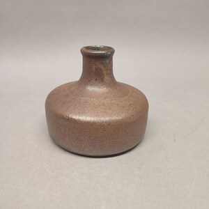 May include: A small, brown ceramic vase with a rounded body and a narrow neck. The vase has a textured surface and a slightly iridescent glaze.