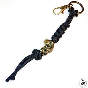 Peut inclure: Porte-clés en paracorde noir avec un charme d'octopus en laiton. Le porte-clés est noué et possède un fermoir métallique.