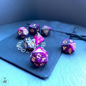 May include: A set of six black and pink dice with gold numbers. The dice are in a black velvet bag with the words "FAYRE MOON" printed on it.