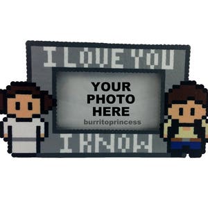 May include: A pixel art photo frame with the text "I LOVE YOU" and "I KNOW". The frame features pixelated characters and the words "YOUR PHOTO HERE". The frame is gray with white lettering and a white background.