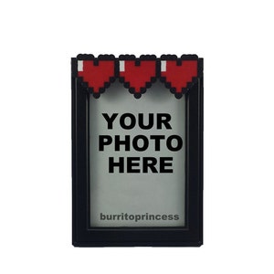 May include: Black photo frame with pixelated red hearts across the top. The frame has the text "YOUR PHOTO HERE" in large, bold letters. The bottom of the frame has the text "burritoprincess".