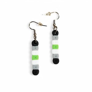 May include: A pair of handmade earrings featuring a design with black, gray, white, and green beads. The earrings have a post and hook closure. The beads are arranged in a vertical pattern, creating a unique and colorful accessory.