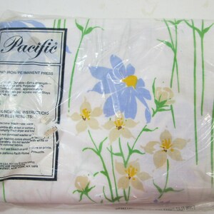 May include: A white sheet with a floral pattern featuring blue and yellow flowers. The sheet is packaged in plastic and has a label that reads "Pacific" and "No Iron/Permanent Press".