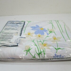 May include: A white flat sheet with a floral pattern in shades of blue, yellow, and green. The sheet is packaged in plastic and labeled "Pacific No Iron Permanent Press" with laundering instructions. The label also states "Flat Sheet for 39x75 in. Mattress".