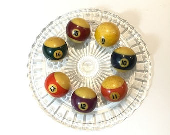 May include: Seven billiard balls on a clear glass plate. The balls are numbered 3, 9, 10, 11, 12, 14, and 15. The balls are yellow, red, green, blue, purple, and black.