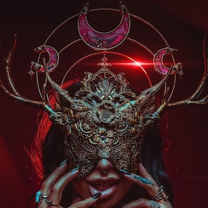 May include: An elaborate gold mask with deer antler features and a crescent moon crown. The mask has detailed floral and filigree patterns. The background is a deep red, creating a dramatic and mystical aesthetic.