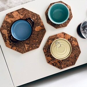 Può includere: Vista aerea di sottobicchieri in sughero con vari oggetti. Una ciotola blu con manici, una ciotola turchese e una lattina dorata sono posizionate sui sottobicchieri. Sono visibili anche calici da vino.