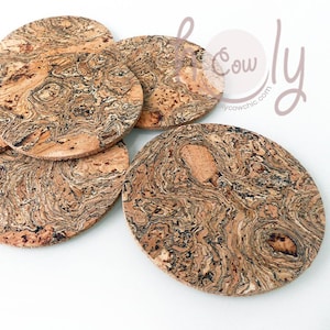 Pode incluir: Um conjunto de cinco bases para copos ovais de cortiça com um padrão natural e rodopiante de tons castanhos claros e escuros. As bases para copos estão dispostas sobre uma superfície branca, mostrando a sua textura e design únicos.