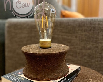 May include: A cork lamp base with a clear glass light bulb on top of two books. The books are titled "Design as Art" and "Design Grafico".