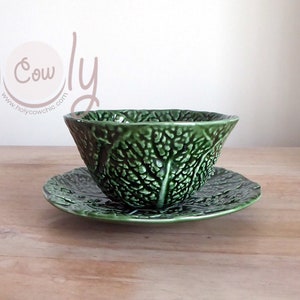 May include: A green cabbage leaf-shaped ceramic bowl and matching plate. The bowl and plate are both decorated with a detailed cabbage leaf design.