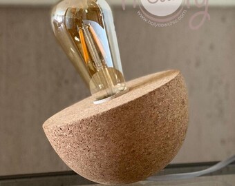 May include: A cork lamp base with a round, half-sphere shape. A clear glass light bulb with a filament is screwed into the base. The lamp is sitting on a white keyboard. The text "holy cow" and "www.holycowchic.com" is visible in the background.