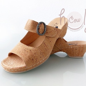 Puede incluir: Sandalias de cuña de corcho con cierre de hebilla. Las sandalias son de color marrón claro y tienen una plataforma de corcho.