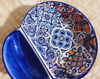May include: A two-section ceramic serving dish with a vibrant blue and white patterned design. The dish has a deep blue, curved handle on one side and a decorative mosaic pattern in shades of blue, white, and orange on the other.