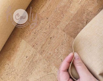 May include: Close-up of a roll of natural cork fabric and a sheet of cork material. The cork has a speckled pattern in shades of brown and tan. The fabric is a light beige color. The image includes the text "Holy Cow" and a website address.