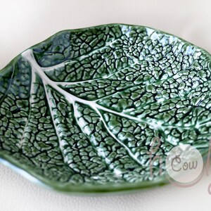 May include: A green ceramic leaf-shaped dish with a white vein design. The dish has a textured surface and a glossy finish. The leaf-shaped dish is a decorative item.