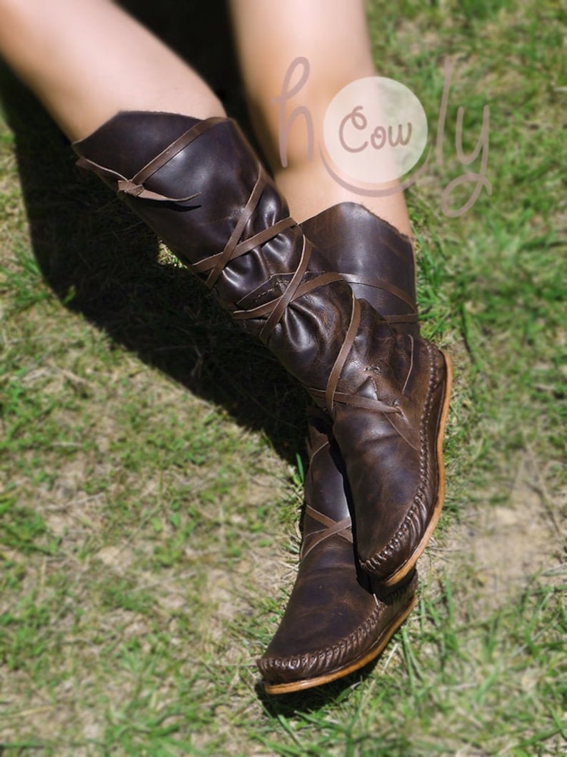 K&ouml;nnte beinhalten: Braune, kniehohe Lederstiefel mit Schn&uuml;rsenkeln und einer dekorativen Naht um die Sohle. Die Stiefel sind abgetragen und haben einen Used-Look.