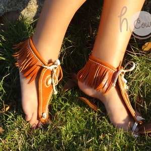May include: A pair of brown leather sandals with fringe detailing. The sandals are tied at the ankle and have a strap that goes between the toes.