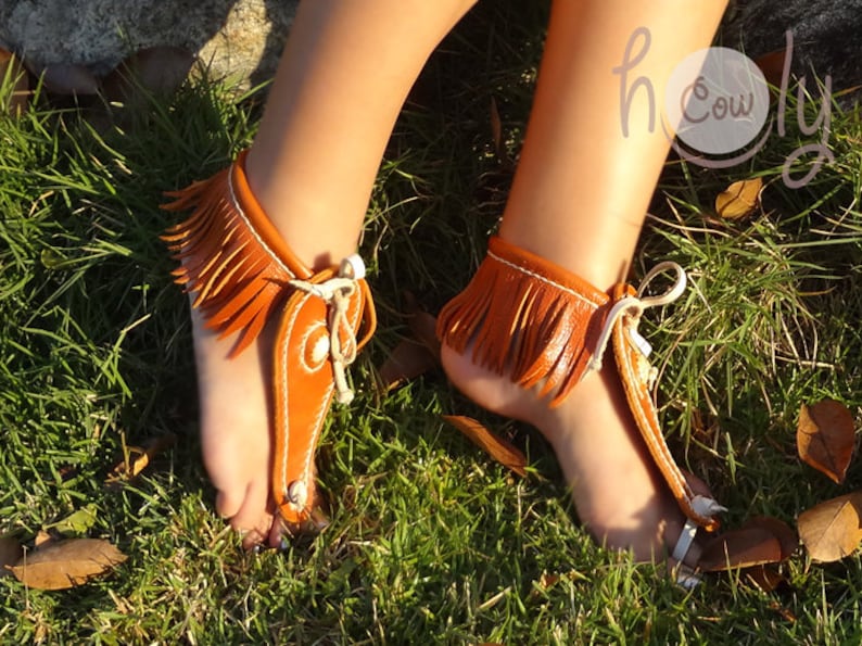 May include: A pair of brown leather sandals with fringe detailing. The sandals are tied at the ankle and have a strap that goes between the toes.