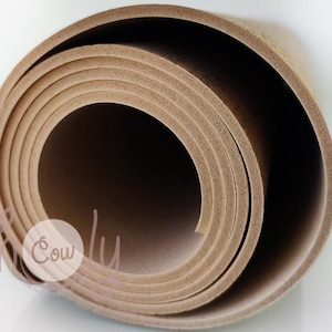 Op de afbeelding: Opgerolde bruine yogamat. De mat is gemaakt van een textuurrijk materiaal en is opgerold in een spiraalvorm. De mat ligt op een witte ondergrond. Het Cowly-logo is zichtbaar in de linker benedenhoek.