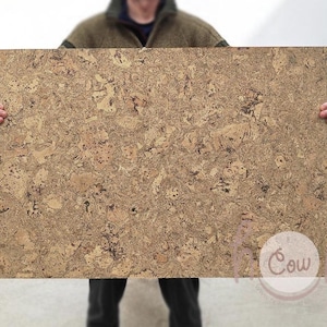 Può includere: Una grande bacheca rettangolare in sughero con un motivo naturale screziato nei toni del marrone e del beige. La bacheca è tenuta da una persona, mostrando le sue dimensioni e la sua consistenza. Ideale per esporre note, foto o altri elementi.