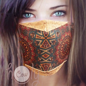 Op de afbeelding: Een vrouw draagt ​​een gezichtsmasker met een kurken buitenkant en een kleurrijk mandala-patroon. Het masker heeft een geometrisch ontwerp in de kleuren rood, oranje, geel, groen en blauw.