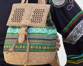 Peut inclure: Petit sac à dos avec une base et un rabat en liège, avec un motif géométrique de découpes en losange. Le corps principal est en tissu coloré avec des rayures et des motifs verts, blancs et rouges. Il a une fermeture à boucle et des bretelles réglables.