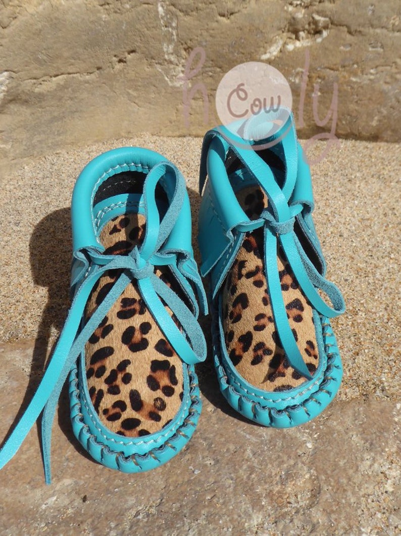 May include: A pair of turquoise leather baby moccasins with leopard print trim and laces.