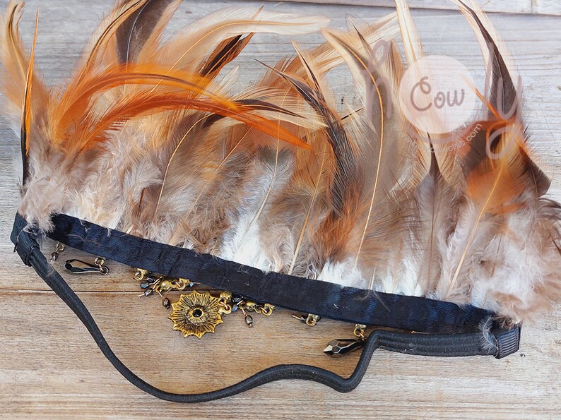 Puede incluir: Una diadema negra adornada con plumas marrones y beige. La diadema presenta una pieza central floral dorada y colgantes. Las plumas est&aacute;n dispuestas en forma de abanico, creando un efecto visual llamativo. Este accesorio es adecuado para eventos tem&aacute;ticos.