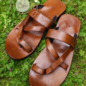May include: Two pairs of brown leather sandals with criss-cross straps. The sandals have a simple design and are made of high-quality leather.