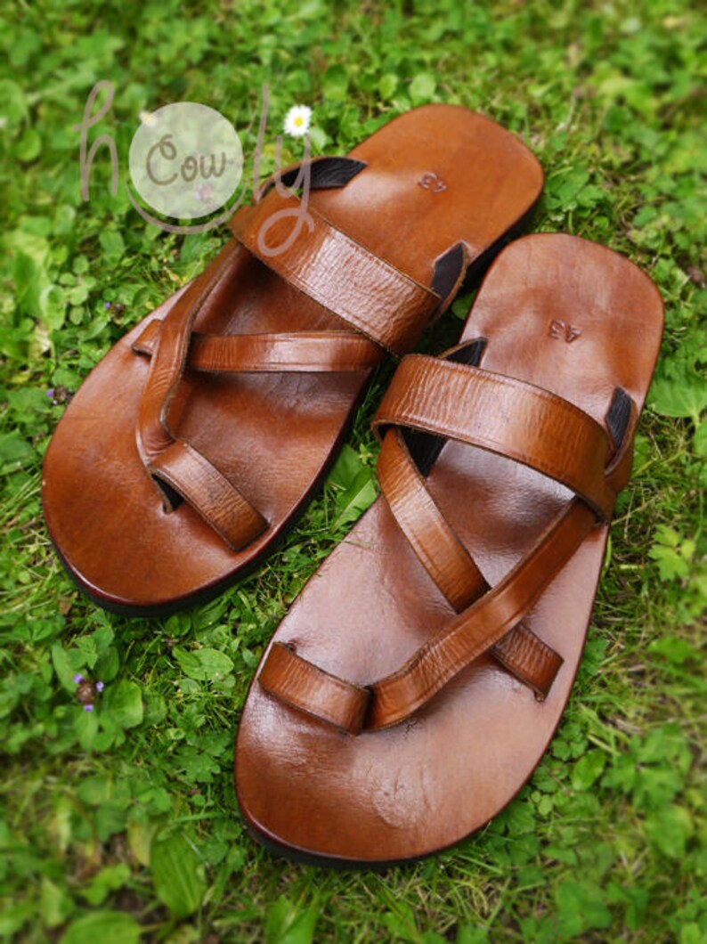 May include: Two pairs of brown leather sandals with criss-cross straps. The sandals have a simple design and are made of high-quality leather.