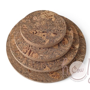 Puede incluir: Un conjunto de cuatro posavasos redondos de corcho, apilados, con un patrón marrón moteado natural. Los posavasos están dispuestos de forma anidada, con el más grande en la parte inferior y el más pequeño en la parte superior. Los posavasos son de corcho.