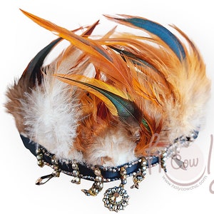 Puede incluir: Tocado decorativo con base de cinta azul oscuro adornada con cristales colgantes y una joya central. Adornado con plumas marrones, blancas y verde azulado, creando un llamativo contraste visual.