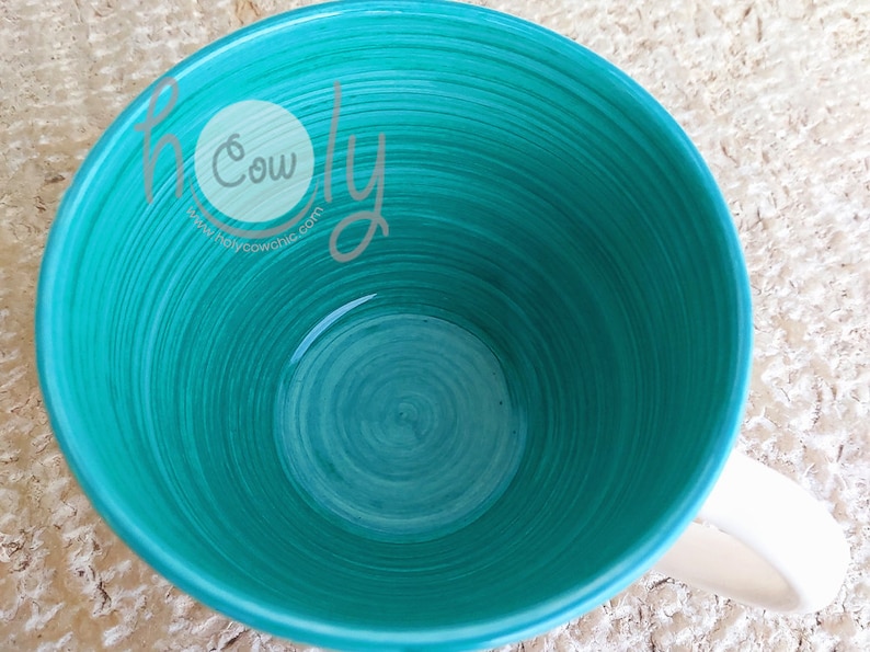 May include: A teal ceramic mug with a white handle. The interior features a spiral design in varying shades of teal. The text "holy cow chic" and a website address are visible on the side of the mug.
