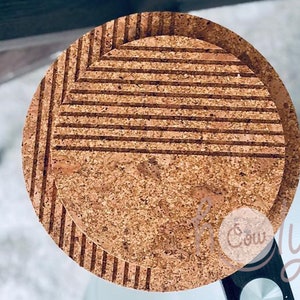 Puede incluir: Dos posavasos redondos de corcho con superficie texturizada. Uno tiene un diseño de chevrón y el otro líneas horizontales. Los posavasos son de color marrón natural y parecen estar hechos de corcho. Están diseñados para proteger las superficies del calor y la humedad.