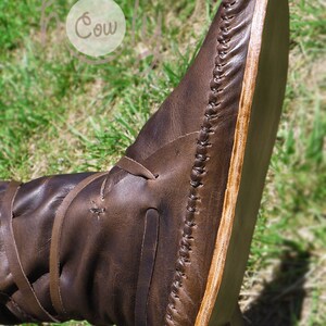 K&ouml;nnte beinhalten: Nahaufnahme eines braunen Lederstiefels mit einer Holzsohle. Der Stiefel hat ein Schn&uuml;rdesign und ist mit einem dicken braunen Faden vern&auml;ht.