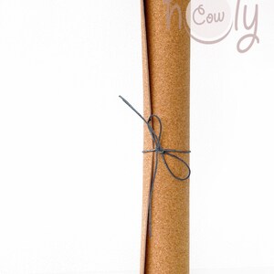 May include: A rolled up cork yoga mat tied with a black string. The mat is brown and has a natural cork texture. The text "holy cow" is written in pink on the mat.