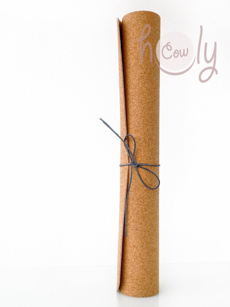 May include: A rolled up cork yoga mat tied with a black string. The mat is brown and has a natural cork texture. The text "holy cow" is written in pink on the mat.